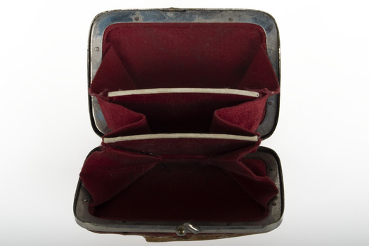 The inside of a purse with silver edging and half clasp, lined in red material and divided into three sections.