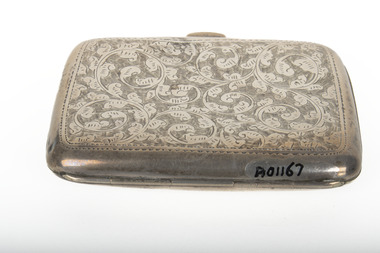 The top of a silver, rectangular cigarette case with rounded corners covered in a swirling floral design that stops at a plain thin border about 1cm from each edge.