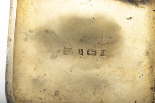 Close-up of the gold washed inside of a silver cigarette case showing four hallmark stamps.