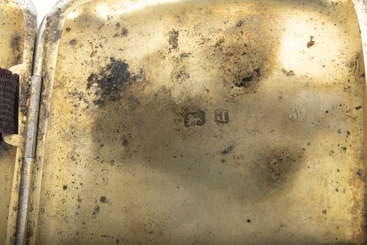 Close-up of the gold washed inside of a  silver cigarette case showing two hallmark stamps.