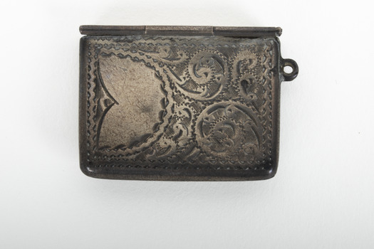 A small sterling silver stamp case with decorative markings inscribed into the metal.