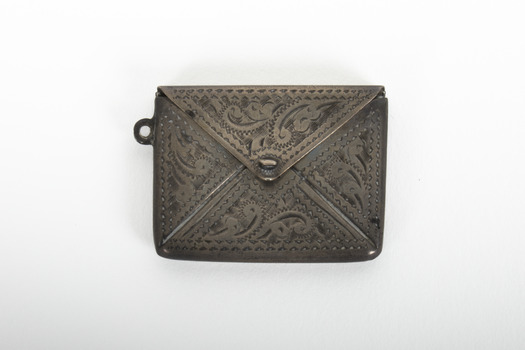 A small sterling silver stamp case with decorative markings inscribed into the metal.