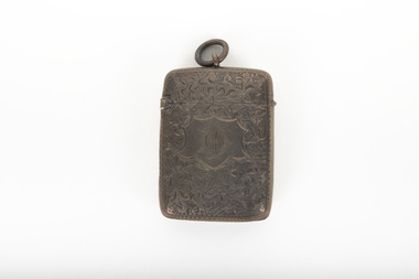A small silver container featuring an engraved design across it's surface and a ring at the top of the lid.