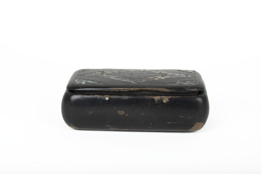 A small black rectangular box with a diamond design on top using small opal coloured flakes