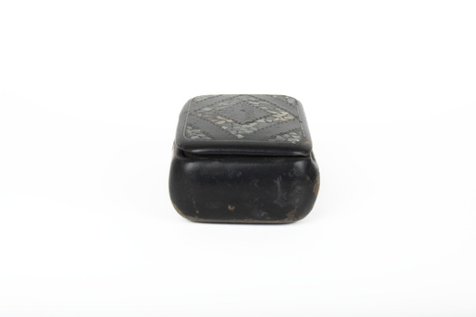 A small black rectangular box with a diamond design on top using small opal coloured flakes