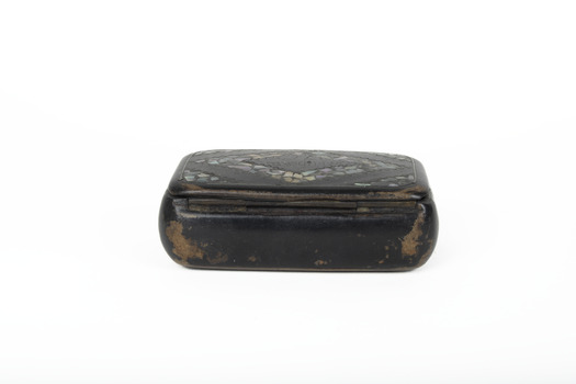 A small black rectangular box with a diamond design on top using small opal coloured flakes
