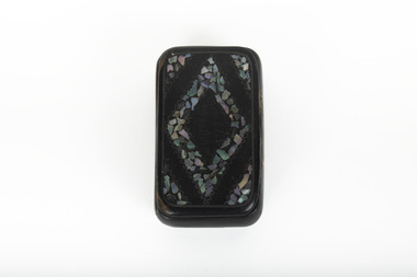 A small black rectangular box with a diamond design on top using small opal coloured flakes