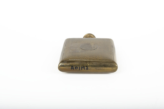 A small lidded square brass bottle embossed with a geometric pattern.