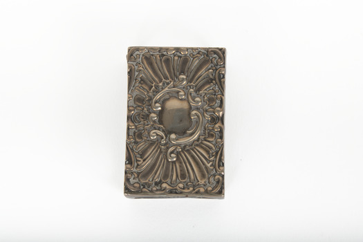 A silver rectangular match case with an embossed top.