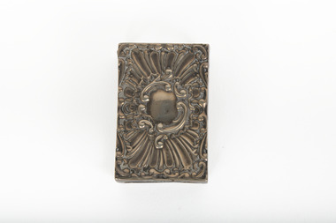 A silver rectangular match case with an embossed top.
