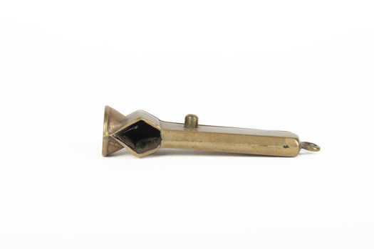 Small bronze metallic cigar cutter positioned on its side exposing front with cigar insert at left side of object. 
