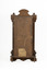 Rear view of a deep brown wooden striking mantle clock showing outline of its decorative features.