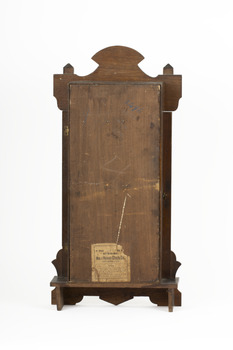 Rear view of a deep brown wooden striking mantle clock showing outline of its decorative features.