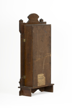 Obverse side view of a deep brown wooden striking mantle clock showing two small golden door hinges.