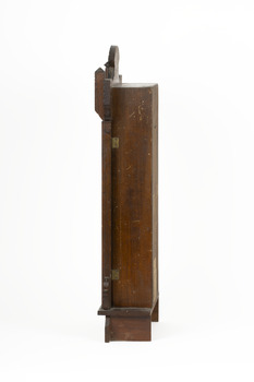 Right side view of a deep brown wooden striking mantle clock showing two small golden door hinges.