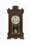 A deep brown wooden striking mantle clock with decorative carvings featuring a glass door with black, gold, and red etched detail. The clock face is white with gold rims and black roman numerals marked.