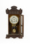 Front view of a deep brown wooden striking mantle clock displayed with its door open. The upper facade and base of the clock feature simple decorative carvings. The open door reveals a gold-toned pendulum mechanism within and a white clock face marked with black roman numerals.
