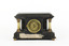 Reverse view of a Seth Thomas black mantle clock with green marbling detail. The Seth Thomas Clock Company logo is laid in a gold-toned door. On either side of the clock are white pillars with bronze-coloured base and top. The clock also features ornate gold claw feet and fine gold painted detailing. A torn maker's label is affixed to the back setting out the name 'Adamantine' and directions to use the clock.  