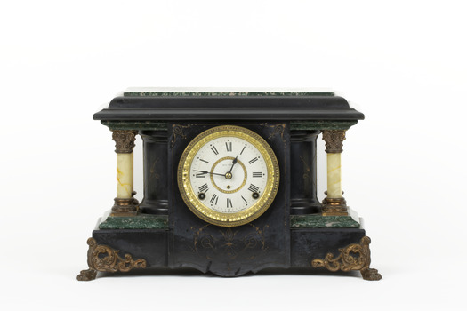 Obverse view of a Seth Thomas black mantle clock with green marbling detail. The clock face is white with black roman numerals and ornate gold rims. On either side of the clockface is a white pillar with bronze-coloured base and top. The clock also features ornate gold claw feet and fine gold painted detailing. 