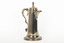 A golden coloured cupro-nickel electroplated hot water jug with a hinged lid, flat base, and elaborate handle.