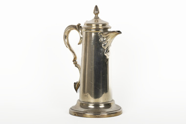 A golden coloured cupro-nickel electroplated hot water jug with a hinged lid, flat base, and elaborate handle.