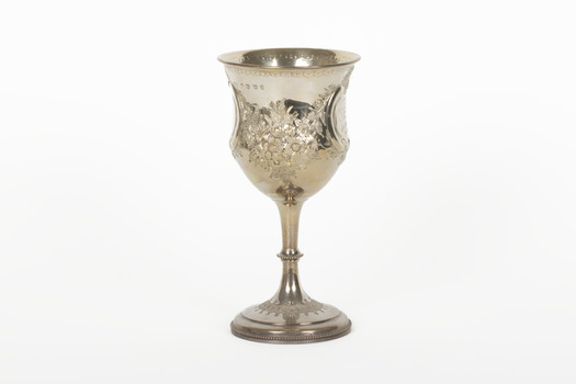 A silver trophy with an engraved flower design going around the cup. A seperate flower deign ring encircles the rim of the cup.