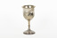 The side angle of a silver trophy. An engraved flower design is visible going around the side of the cup. On the right-hand side of the cup is a swirling deign with a small portion of writing visible.