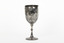 Silver cup in the shape of a wine glass, as the cup tapers to a pedestal. The cup is engraved with branches and leaves, the base engraved with lines, dots and a half-moo pattern. 