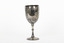 Silver cup in the shape of a wine glass, as the cup tapers to a pedestal. The cup is engraved with branches and leaves, the base engraved with lines, dots and a half-moo pattern. 