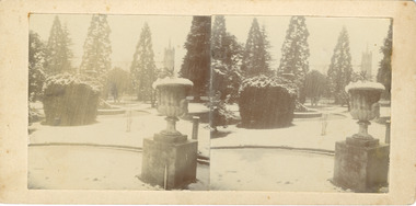 A stereoscopic photograph mounted on card depicting Town Hall Gardens covered in snow. A fountain is at the centre, with a fluted garden urn and a tap stand in the foreground. A row of trees line the background with a church steeple visible in the distance.  