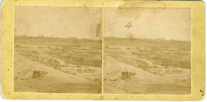 Two square faded sepia toned photos of a landscape with a bridge made of an unsealed gravel road in the foreground. Some trees, small buildings, roads and fences in the background.