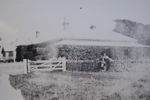 Two people sitting on dry stone wall in front of a bluestone homestead covered with ivy.  