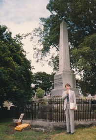 Man in suit standing in front of a tall monument in the shape of an obelisk 