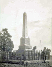First Nations man wearing tribal dress standing in front of tall stone monument