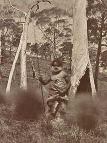 Bearded First Nations man dressed in possum skin cloak holding a spear