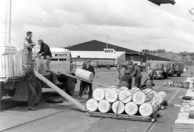 Photograph, Cylindrical containers (wood pulp?) being unloaded from a small truck, n.d