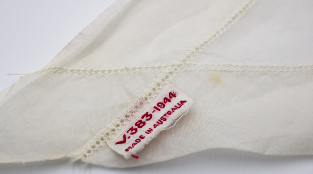 Detail of manufacturer's label stitched into hem of white headscarf. White label with red cotton stitching