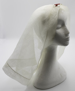 Triangle shaped scarf with Red Cross in centre front. On white foam mannequin head, with white background. Shows translucent nature of fabric.