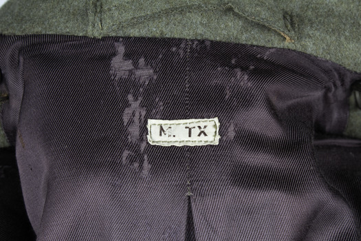 Sewn manufaturer's label at the inside nap of coat with purple lining. Rectangle, white label with black text reads: M.TX