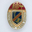 Oval shaped badge with Australian coat of arms on top, blue shield centre, and with white edge with gold writing.
