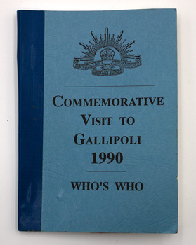 Blue cardboard cover of booklet with black text and blue tape binding on the spine. Rising Sun emblem at top followed by text: Commemorative Visit To Gallipoli 1990: Who's Who