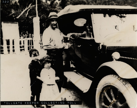 Tollkeeper collecting toll from car driver with two children beside him