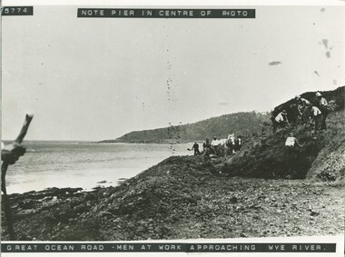 Men at work on Great Ocean Road nearing Wye river with pier visible behind them