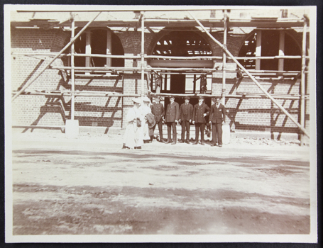 Sepia photograph depicting two ladies and 5 crew members/officers standing in front of the Siddeley Street mission in construction (scaffholdings) around 1906. 