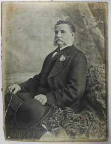 Man seated holding a bowler hat in his left hand and a cane in his right hand