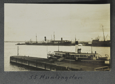 Small landscape sepia photograph of two vessels in the foreground a ferry or coaster moored at small wooden quay and in the distance moored at a pier an ocean going steamship with one stack or funnel.