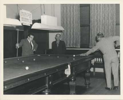 Three men playing pool on a large billiard table in the Billiard Room of the Flinders St Mission
