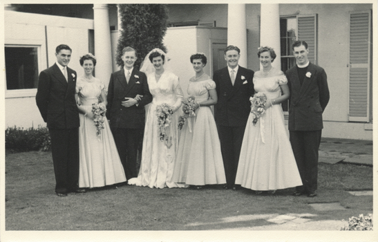 A group photograph depicting a bride and groom with their bridesmaids, groomsmen and priest.