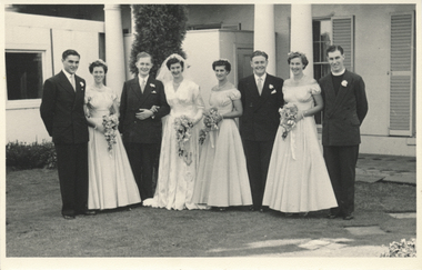 A group photograph depicting a bride and groom with their bridesmaids, groomsmen and priest.