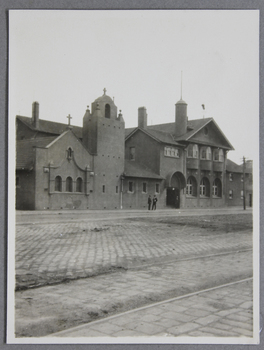 Small photograph depicting the Mission from Flinders Street East West on a slight angle; two men are standing in front of the building.